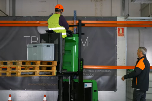 imagen de una operario de logística, con casco, en un almacén cargando una caja.